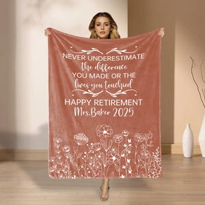 May include: A terracotta blanket with white text: "NEVER UNDERESTIMATE the difference YOU MADE OR THE lives you touched HAPPY RETIREMENT Mrs. Baker 2025." A white floral pattern decorates the bottom edge of the blanket.