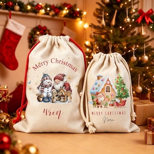 Könnte beinhalten: Zwei beige Geschenksäcke mit Kordelzug aus Stoff. Der größere Sack zeigt einen Schneemann, den Weihnachtsmann und Waldtiere mit dem Text Merry Christmas und dem Namen Wren. Der kleinere Sack zeigt ein Haus, den Weihnachtsmann und Elfen.