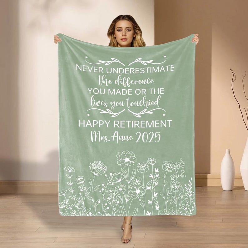 May include: A sage green blanket with white text reading: "NEVER UNDERESTIMATE the difference YOU MADE OR THE lives you touched HAPPY RETIREMENT Mrs. Anne 2025." Features a floral border design.