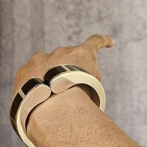 May include: A gold and black bangle bracelet with a unique design. The bracelet is made of two curved pieces that fit together.