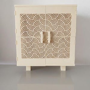 Peut inclure: Un meuble crème avec un motif géométrique en forme de vagues sur les portes. Le meuble a deux portes avec deux poignées et repose sur quatre petits pieds. Le motif de vagues est répété sur les portes.