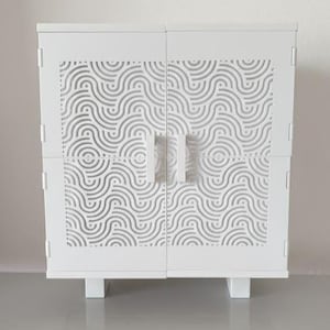 May include: A white cabinet with a wave pattern design on the doors. The cabinet has two handles and stands on four short legs. The doors are divided into four sections. The cabinet is made of wood.