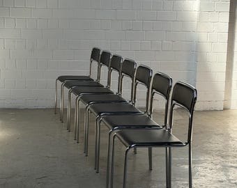May include: A row of six identical chairs featuring polished chrome metal frames and black upholstered seats and backrests. Each chair has a simple four-legged design with a continuous tubular metal structure forming the frame and back support.