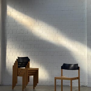 Peut inclure: Chaises en bois avec dossiers noirs empilées et disposées devant un mur de briques blanches. Une chaise est seule. Les chaises ont un design simple et moderne avec une finition en bois naturel.