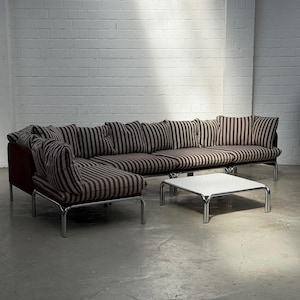 May include: A modular sectional sofa featuring dark brown and cream vertical striped upholstery with a deep red side panel, supported by a chrome metal frame. A matching square coffee table with a white top and chrome legs sits in front.