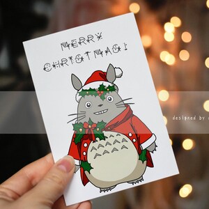 Może przedstawiać: Biała kartka świąteczna z postacią z kreskówki ubraną w strój i czapkę Świętego Mikołaja, z napisem "MERRY CHRISTMAS!" w kolorze czarnym. Postać jest szara z białym brzuchem i ozdobiona ostrokrzewem.