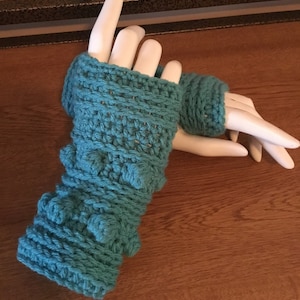 May include: A pair of teal blue crocheted fingerless gloves with a textured design. The gloves have a raised, bumpy texture on the bottom half of the gloves.