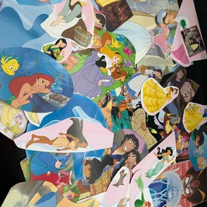 May include: A collection of colorful Disney princess character cutouts, including Ariel, Belle, Cinderella, Snow White, and Pocahontas. The cutouts are arranged in a random pattern on a dark surface.