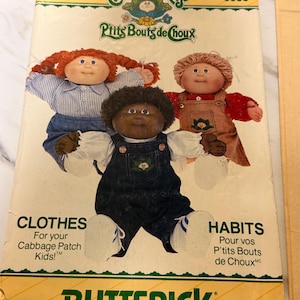 May include: A vintage Butterick sewing pattern for Cabbage Patch Kids clothes and habits. The pattern features illustrations of three Cabbage Patch Kids dolls. The text includes "Clothes" and "Habits" in English and French.