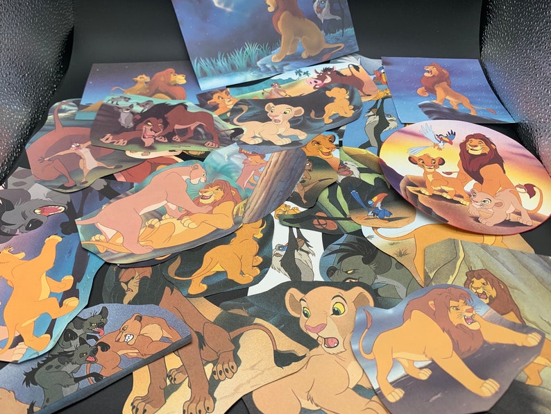 May include: A collection of colorful cartoon lion character cutouts, featuring various poses and expressions. The cutouts are arranged in a pile, with some overlapping. The characters are all from the Disney movie The Lion King.