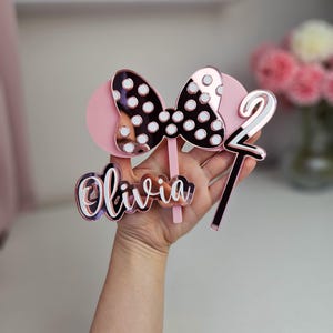 May include: Pink and white polka dot bow with a rose gold mirror finish, a pink and white number two, and a rose gold mirror finish name Olivia.