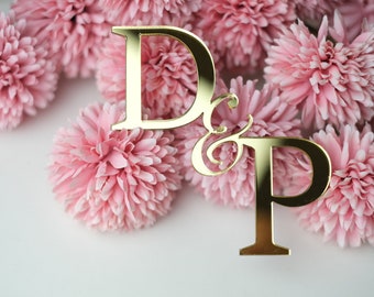 May include: Gold D & P wedding cake topper with a decorative script ampersand, surrounded by pink silk flowers.
