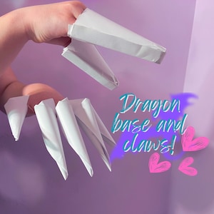 May include: White paper dragon claws and base for finger puppets. The text "Dragon base and claws!" is written in teal on a purple background with pink hearts.