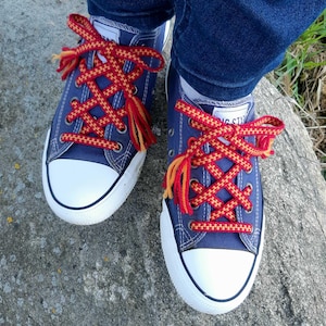 May include: A pair of blue canvas trainers with red and yellow shoelaces tied in a criss-cross pattern.