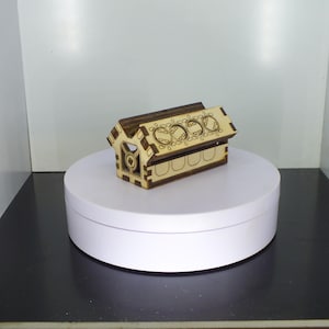 Peut inclure: Une petite boîte en bois en forme de maison avec un motif décoratif sur le dessus et une finition en bois brun.