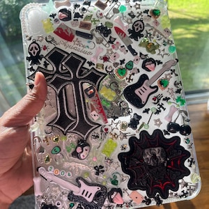 May include: A clear plastic case with a black and white cross, a black and white guitar, a black and red skull, and other small black and white charms. The case is filled with a clear resin and has a glittery finish.