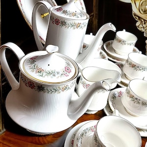 May include: A white porcelain tea set with a floral pattern. The set includes a teapot, creamer, sugar bowl, and four teacups and saucers.