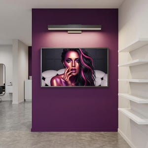 May include: A framed artwork of a woman with pink and black hair, mounted on a deep purple wall. A rectangular light fixture is positioned above the artwork. White shelves are on the right. The room has a modern aesthetic.