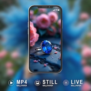 May include: A smartphone displays a wallpaper featuring a large, oval-cut blue gemstone ring. The ring is set on a dark surface with pink flower petals and a blurred floral background. The phone has the words "MP4 WALLPAPER", "STILL WALLPAPER", and "LIVE WALLPAPER" at the bottom.