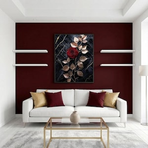 May include: A framed artwork featuring a red rose with gold-colored leaves against a dark marble background. The artwork hangs above a white sofa with decorative pillows. The room has burgundy walls and white shelves.
