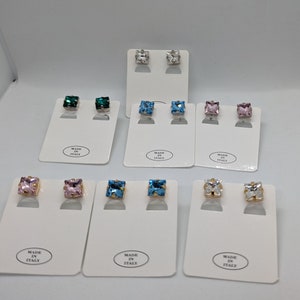 May include: Assortment of square stud earrings with various colored gemstones. The earrings are displayed on white cards with the text "Made in Italy".