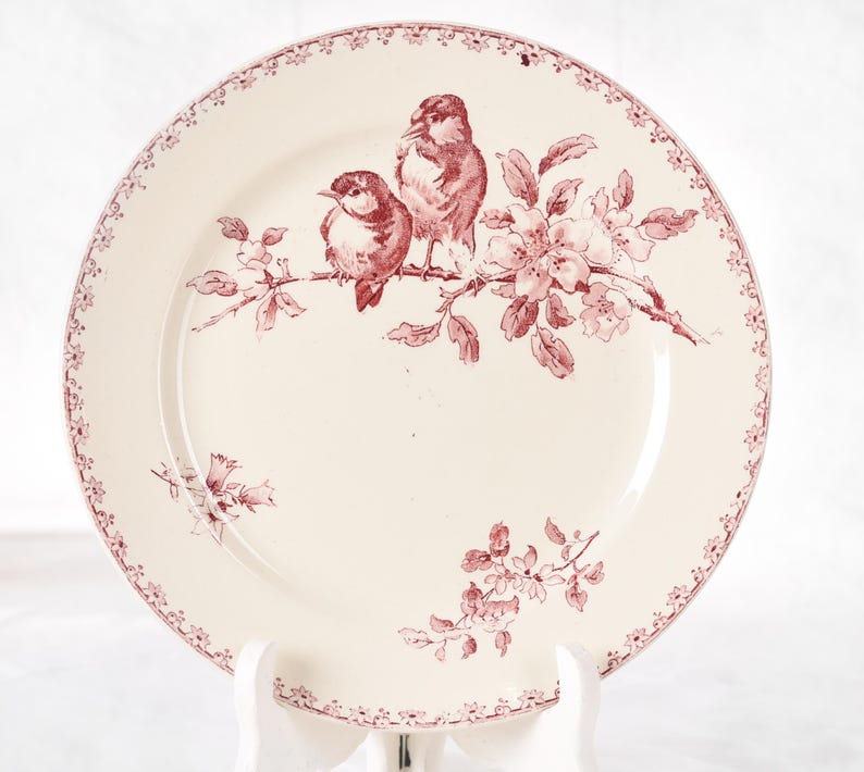 Puede incluir: Plato de cer&aacute;mica color crema con un dise&ntilde;o de p&aacute;jaros y flores en color granate. Dos p&aacute;jaros se posan en una rama con flores. El borde del plato tiene un borde floral granate. Una pieza decorativa para la cocina o el comedor.
