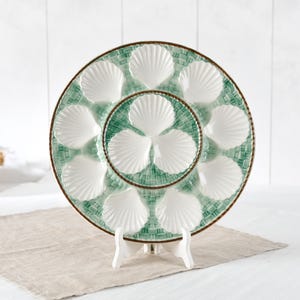 Peut inclure: Une assiette à huîtres ronde en céramique avec un motif de vannerie vert et blanc. L'assiette présente douze empreintes blanches en forme de coquille disposées en cercle, avec neuf sur le bord extérieur et trois au centre.