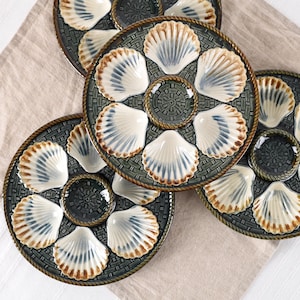 May include: Three round ceramic oyster plates featuring a dark green woven basket-weave pattern background. Each plate has six molded shell-shaped indentations with cream and blue-grey glaze, surrounding a central circular well with a rope border.