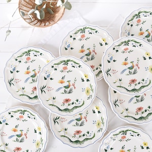 Peut inclure: Ensemble d'assiettes en céramique blanche avec un bord festonné et une bordure bleue. Chaque assiette présente un motif coloré d'oiseaux et de fleurs. Les assiettes sont disposées sur une surface blanche.