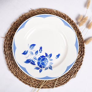 Peut inclure: Une assiette en céramique blanche avec un motif floral bleu et blanc. L'assiette est posée sur un dessous de plat en paille tressée.