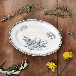 Könnte beinhalten: Eine weiße ovale Servierplatte mit einem blauen und weißen Blumendesign. Die Platte hat einen gewellten Rand und ist mit einem sich wiederholenden Muster aus Blumen und Blättern verziert.