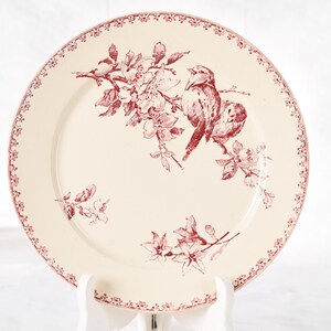 Puede incluir: Plato de cer&aacute;mica color crema con un dise&ntilde;o floral y de p&aacute;jaros en color granate. El plato presenta una ilustraci&oacute;n detallada de dos p&aacute;jaros posados en una rama florecida. El borde est&aacute; decorado con un delicado borde floral, a&ntilde;adiendo elegancia.