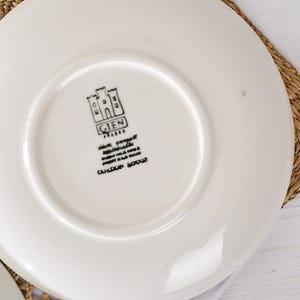 Puede incluir: Plato de cer&aacute;mica blanca con logotipo y texto en negro. El logotipo presenta un dise&ntilde;o de castillo con la palabra "GIEN" encima del texto. El plato est&aacute; sobre una estera tejida.