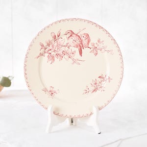 Puede incluir: Plato de cer&aacute;mica color crema con dise&ntilde;o floral y de p&aacute;jaros rojos. El plato presenta dos p&aacute;jaros posados en una rama florecida, con un delicado borde punteado. Una pieza decorativa para servir o exhibir.