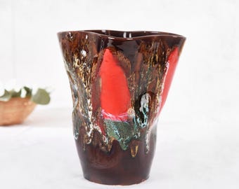 May include: A tall, ceramic vase with a unique, organic shape. The vase features a rich, dark brown base that transitions to a vibrant red and brown upper section. The textured surface has accents of white, green, and gold.