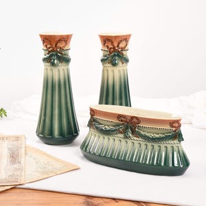 Peut inclure: Ensemble de trois vases en céramique vert et brun avec un motif décoratif de ruban et de feuilles. Les vases sont de tailles et de formes différentes.