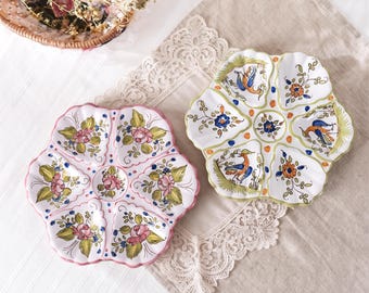 May include: Two ceramic serving platters with a scalloped edge and six compartments. One platter features hand-painted pink roses and green leaves, while the other displays blue and orange birds and floral motifs on a white glazed background.