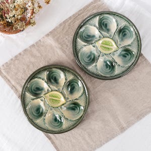 May include: Two round ceramic oyster plates featuring a textured dark green rim and six individual shell-shaped indentations surrounding a central yellow lemon-shaped compartment for serving seafood, finished with a glossy glaze.