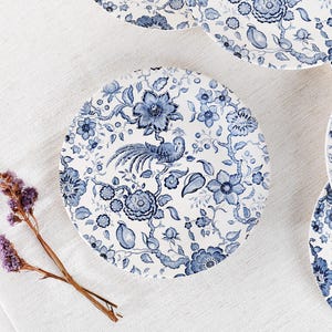 Puede incluir: Un plato de cerámica blanco con un patrón floral azul y blanco. El patrón presenta un pájaro con una cola larga, flores y hojas.