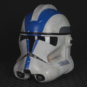 May include: A white and blue helmet with a weathered appearance. The helmet features blue stripes and accents, with a dark visor and two circular lenses at the bottom. The design suggests a futuristic or science fiction theme.