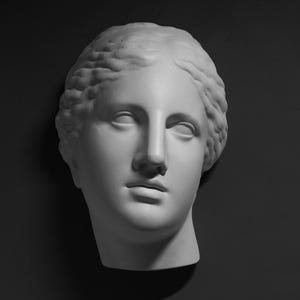 Könnte beinhalten: Ein weißer Gipsabguss eines Frauenkopfes mit detaillierter Frisur. Die Skulptur ist ein klassisches Beispiel für eine Porträtbüste.
