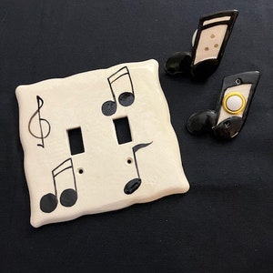 May include: A white ceramic light switch cover with black musical notes and a treble clef. Two matching black ceramic light switch covers with white musical notes are also included.