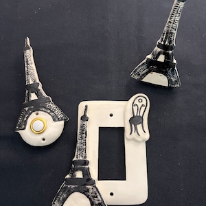 May include: Three white ceramic light switch covers with black Eiffel Tower designs. One cover features a black and white chair design.