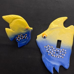 May include: Two ceramic light switch covers shaped like yellow and blue fish with black and white polka dots. The fish have a light switch opening in the center.