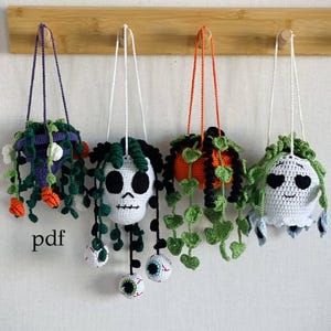 Könnte beinhalten: Vier hängende Häkel-Pflanzenhalter mit gruseligen Halloween-Themen. Jeder hat ein einzigartiges Design, darunter ein Totenkopf, ein Kürbis und andere skurrile Elemente. Die Pflanzen sind an einer Holzstange mit weißen Kordeln aufgehängt. Das Wort "pdf" ist sichtbar.