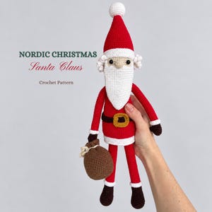 Puede incluir: Un muñeco de Papá Noel tejido a ganchillo con traje rojo, barba blanca y gorro puntiagudo con pompón blanco. El muñeco lleva un cinturón marrón con hebilla amarilla y botas marrón oscuro, sosteniendo un saco marrón. Texto: NORDIC CHRISTMAS Santa Claus Crochet Pattern.