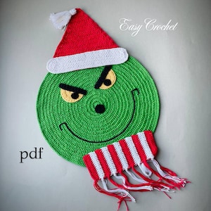 May include: A crocheted green circle with a face, wearing a red and white Santa hat and a red and white striped scarf. The face has black eyebrows, yellow eyes, and a black nose and smile. The word "pdf" is in the lower left corner, and "Easy Crochet" is in the upper right.