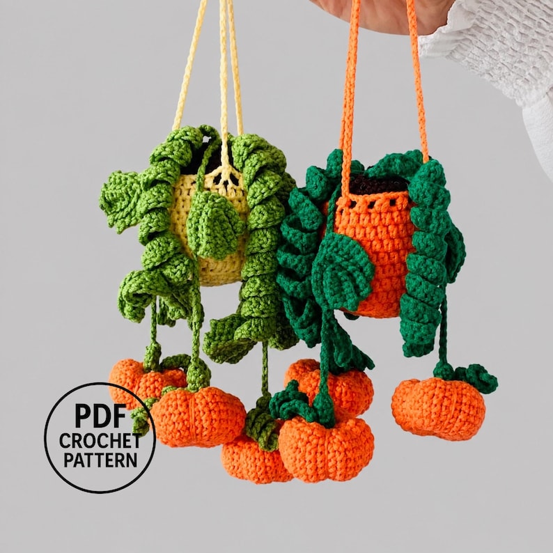 May include: Two hanging crochet plant baskets with yellow and orange pots. Each basket features long, trailing green vines with small orange pumpkin-shaped accents. A circular black logo with the text PDF CROCHET PATTERN is in the corner.