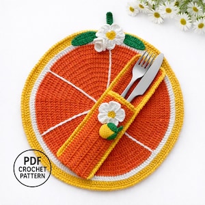 Könnte beinhalten: Ein gehäkeltes Platzset in Form einer Orangenscheibe und ein passender Besteckhalter. Das Platzset ist orange mit weißen und gelben Akzenten sowie einer weißen Blumen- und Zitronenverzierung. Eine Gabel und ein Messer befinden sich im Halter. Der Text "PDF CROCHET PATTERN" befindet sich unten links.