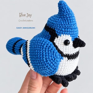 Può includere: Un uccellino amigurumi all'uncinetto a forma di ghiandaia azzurra, realizzato con filato blu brillante, bianco e nero, con una cresta appuntita, occhi di sicurezza neri e un becco nero. Il testo sull'immagine recita Blue Jay Crochet pattern EASY AMIGURUMI.